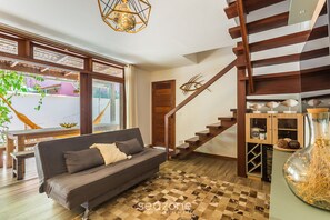 A modern living room with a sofa, wooden staircase, and a large window with a view of the outside. - Apt w/ Gourmet Area & BBQ in Marau Cvb0126 (Maraú)