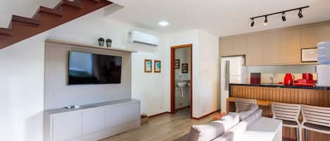 A modern living room with a flat-screen TV, a sofa, and a staircase.