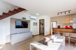 A modern living room with a flat-screen TV, a sofa, and a staircase. - Apart in Condo w/ Barbecue Grill and Pool Cvb0110 (Maraú)