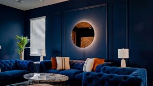 A dark blue living room with a sectional sofa, round coffee table, and a round wall feature. - Private Theater, Themed Rooms & Hot Tub (Davenport)