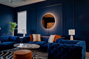 A dark blue living room with a sectional sofa, round coffee table, and a round wall feature. - Private Theater, Themed Rooms & Hot Tub (Davenport)