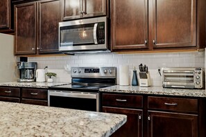 A kitchen with dark wooden cabinets, a stainless steel microwave, a coffee maker, a toaster, and a dishwasher. - Private Theater, Themed Rooms & Hot Tub (Davenport)