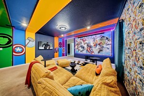 Ein gemütliches Zimmer mit einem großen Flachbildfernseher, bequemen Sitzmöglichkeiten und einer Wand, die mit Comic-Aufklebern verziert ist.