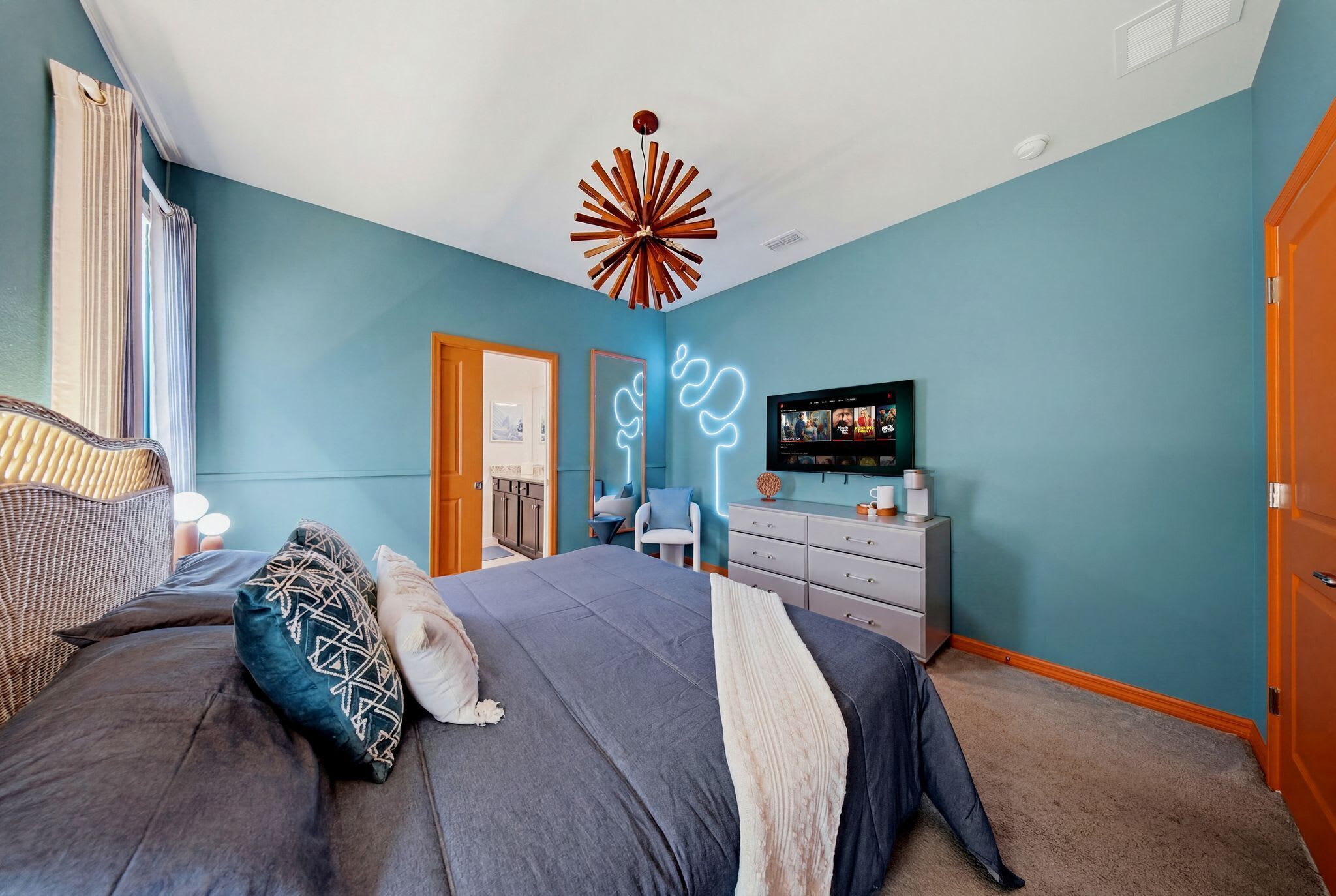 A bedroom with a bed, dresser, television, and a unique ceiling light fixture.