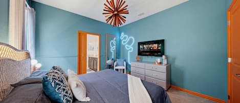 A bedroom with a bed, dresser, television, and a unique ceiling light fixture.