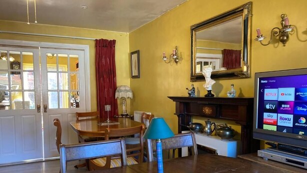 A living room with a dining table, chairs, a blue lamp, a fireplace, a television, and a large mirror on the wall. - Hotel Jacks Court (Ashton-under-Lyne)