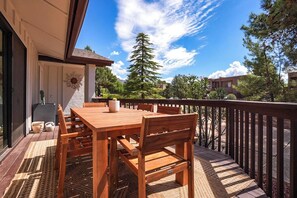 Eine Terrasse im Freien mit einem Holztisch und -stühlen, einem Blumentopf sowie Blick auf einen Berg und Bäume.