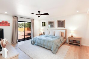 Ein Schlafzimmer mit Bett, Deckenventilator, Nachttisch, Lampe und Blick ins Freie.