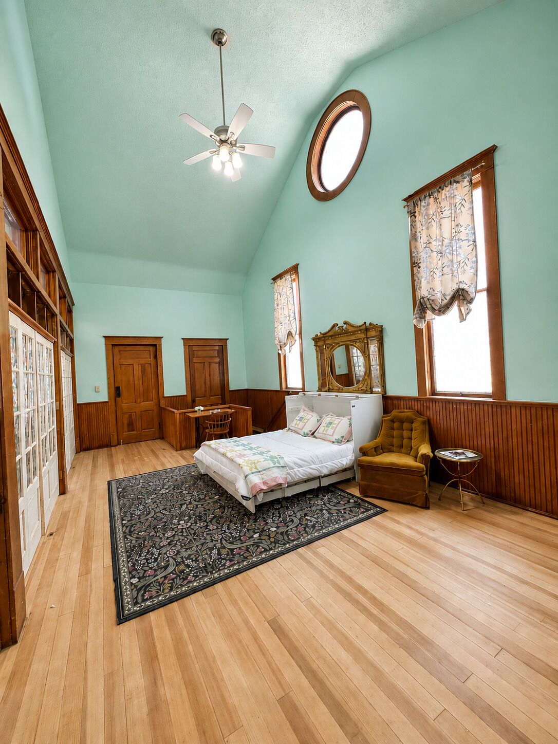 A bedroom with a bed, a chair, a desk, a mirror, and a ceiling fan.