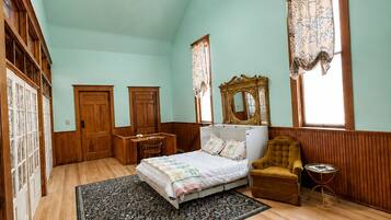 A bedroom with a bed, a chair, a desk, a mirror, and a ceiling fan.