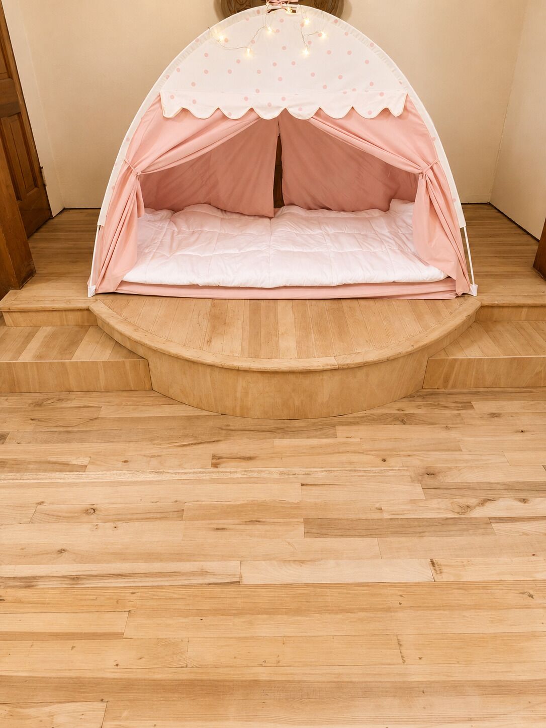 Una estructura tipo tienda con borde ondulado y techo blanco con lunares rosas, sobre un suelo de madera con base curva.