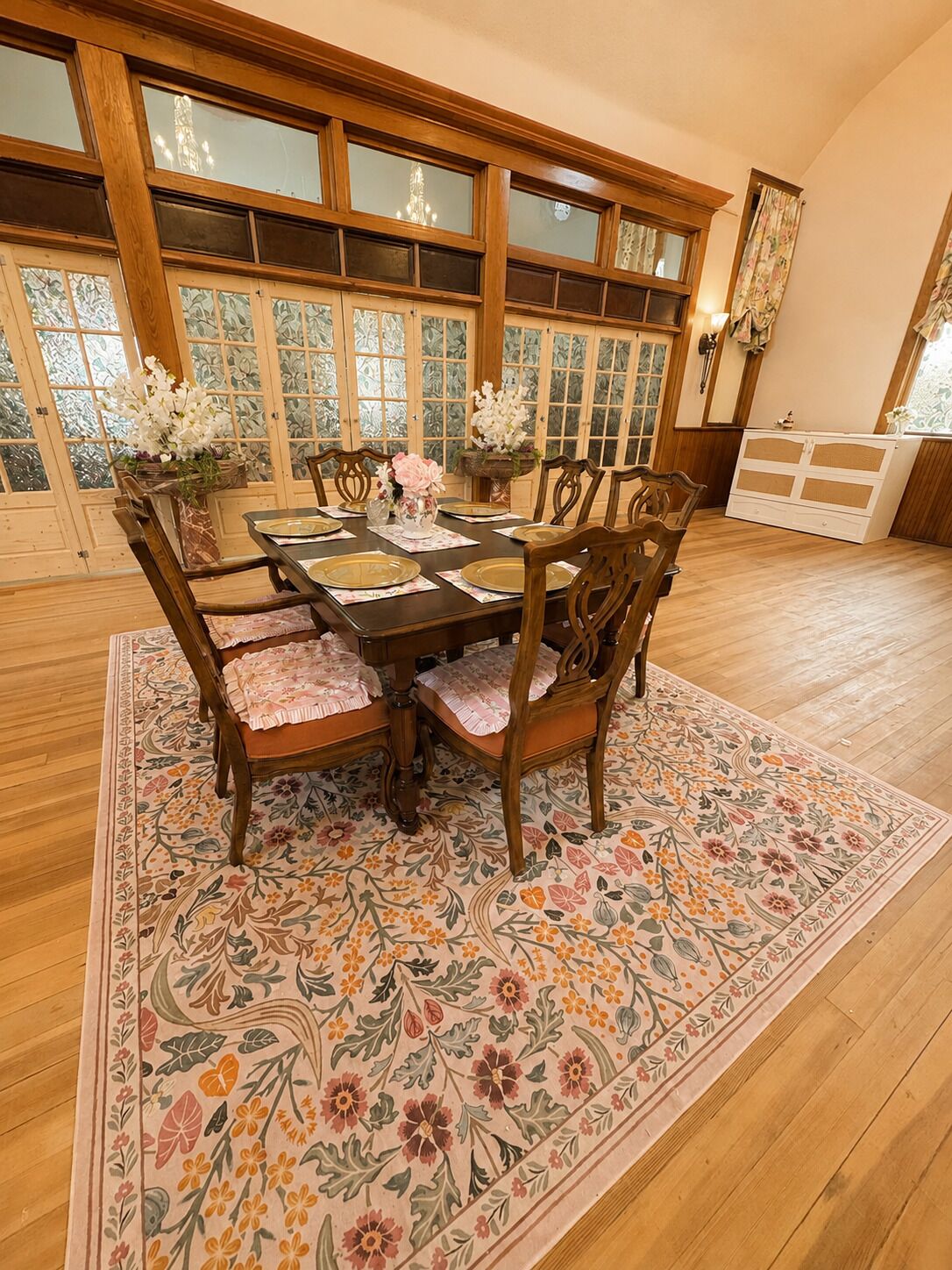 A dining area with a wooden table set for six, surrounded by chairs with floral cushions.