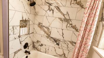 A bathroom with a marble-tiled wall, a bathtub, a showerhead, and a floral shower curtain.