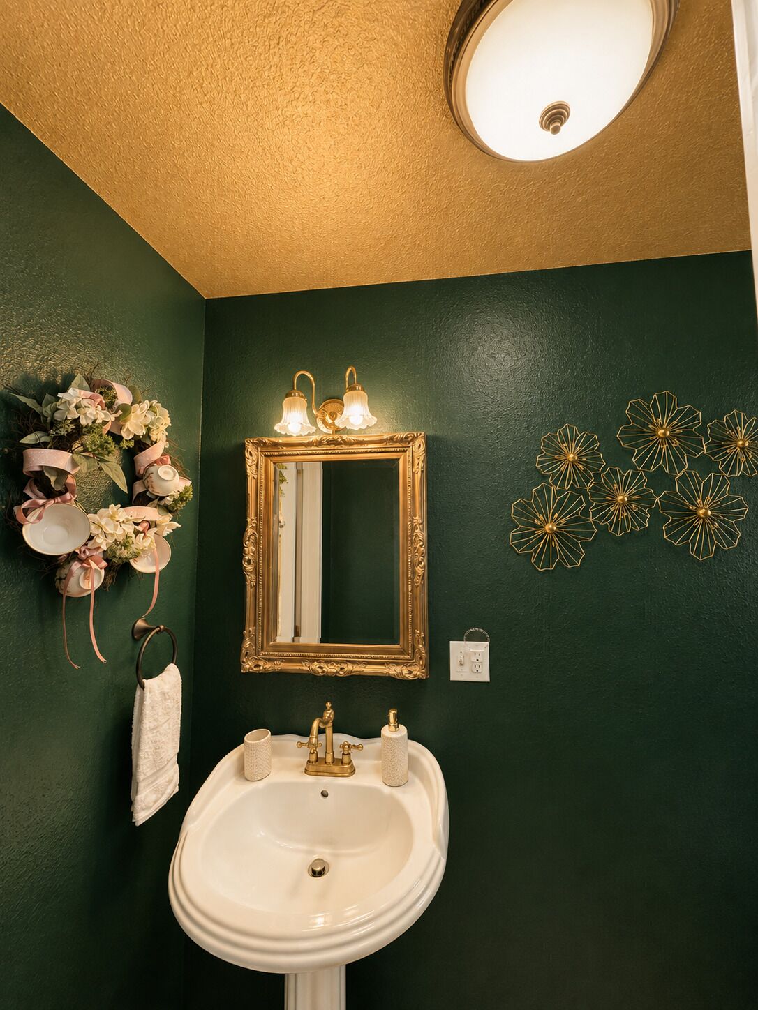 A bathroom with a white sink, a gold-framed mirror, and decorative wall art.