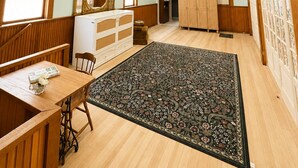Een kamer met een houten bureau, een stoel, een bed, een kledingkast en een plafondventilator.
