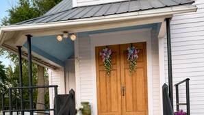 Een huis met een veranda, dubbele houten deuren en een trap naar de ingang.