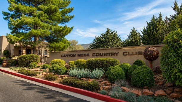 A building with a sign reading 'Canyon Mesa Country Club' surrounded by landscaped gardens and a large decorative sculpture. - Sedona Single-Level · Remodeled, Two Kings, Red Rock Views, Tennis, Pool & Golf (Sedona)