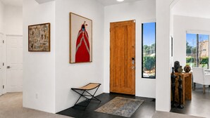 A hallway with a wooden door, a framed artwork, a folding chair, and a view of the outdoors through a window. - Sedona Single-Level · Remodeled, Two Kings, Red Rock Views, Tennis, Pool & Golf (Sedona)