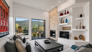 A modern living room with a sofa, coffee table, and a fireplace. There is a balcony with a view of the hills. - Sedona Single-Level · Remodeled, Two Kings, Red Rock Views, Tennis, Pool & Golf (Sedona)