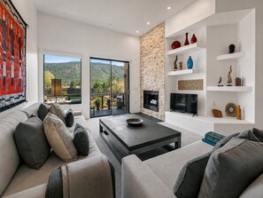 Ein modernes Wohnzimmer mit Sofa, Couchtisch und Kamin. Ein Balkon bietet Blick auf die Hügel.