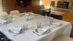 Un coin repas agrémenté d’un mur en pierre, d’une cheminée et d’une table dressée pour six personnes, avec des nappes blanches et de la verrerie.