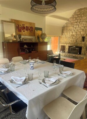 Un coin repas agrémenté d’un mur en pierre, d’une cheminée et d’une table dressée pour six personnes, avec des nappes blanches et de la verrerie.