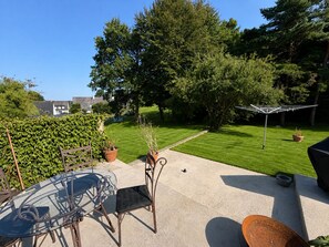 A patio area with a glass table and chairs, a metal chair, a lawn, and a clothes drying rack.