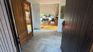Un couloir avec une armoire en bois, un sol carrelé et une vue sur un espace de vie comprenant un canapé et un tapis.
