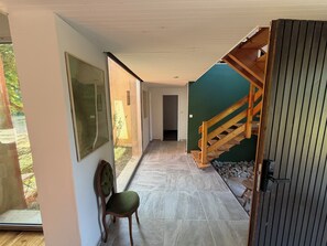 A hallway with a chair, a wooden staircase, and a door leading to a room.