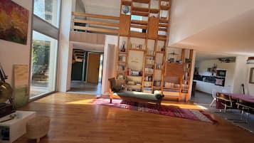 Uma sala ampla com piso de madeira, um sofá, uma estante e um espaço de jantar com cadeiras.