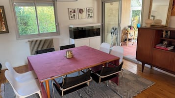 Un comedor con una mesa, sillas, un radiador y vistas a través de un ventanal.