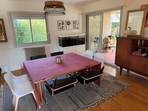 Uma área de refeições com mesa, cadeiras, um radiador e vista através de uma porta de vidro.