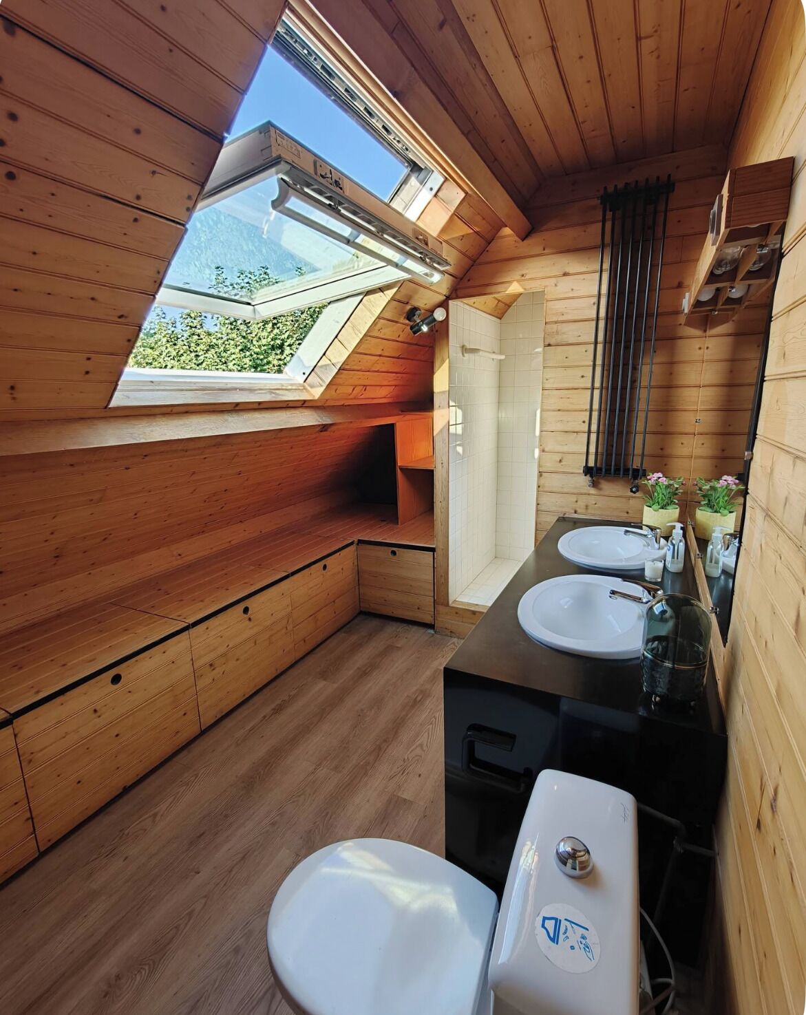 Une petite cabane en bois avec un puits de lumière, une petite salle de bain comprenant des toilettes et un lavabo.