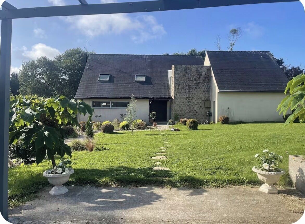 A house with a paved driveway leading to a garage, surrounded by a well-maintained lawn and potted plants.