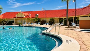 Une piscine avec, en arrière-plan, un bâtiment surmonté d’un toit rouge, entouré de chaises longues et de palmiers.