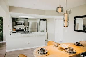 A modern kitchen with stainless steel appliances, a white countertop, and a dining area with a wooden table and woven placemats. - Luxury Townhome 15 min to Disney Universal Orlando (Davenport)