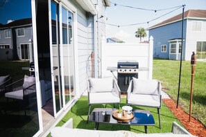 A backyard with a barbecue grill, two white chairs, a small table with a tray, and a glass door leading to a patio. - Luxury Townhome 15 min to Disney Universal Orlando (Davenport)