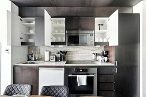 Una cocina moderna con electrodomésticos integrados, estanterías abiertas y un comedor con mesa y sillas.