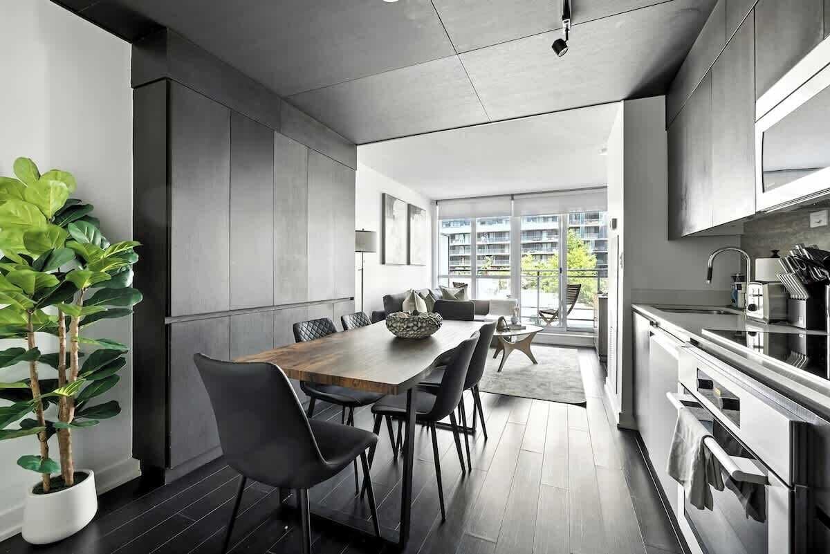 A modern kitchen with a dining area, large windows, and a view of a residential building.