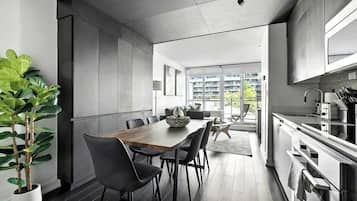 A modern kitchen with a dining area, large windows, and a view of a residential building.