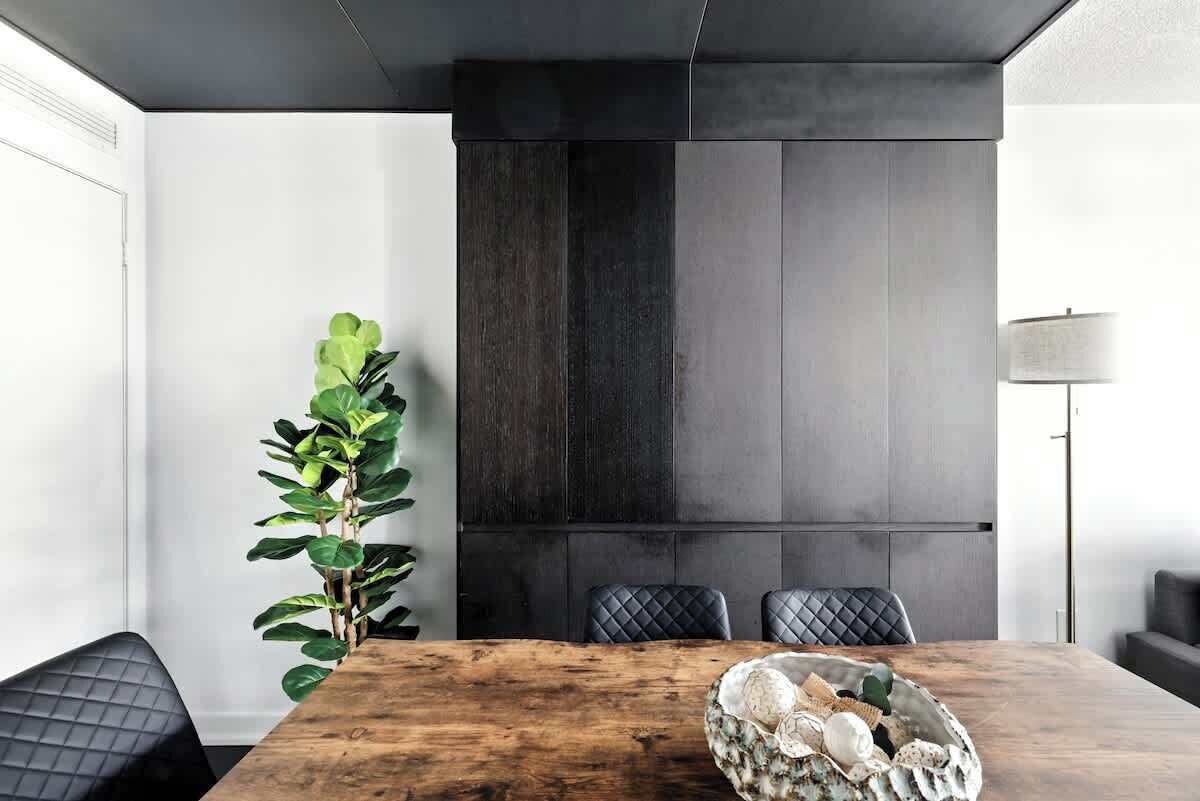 Un espace repas moderne avec une table en bois, des chaises à revêtement noir et une grande plante.