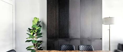 Un espace repas moderne avec une table en bois, des chaises à revêtement noir et une grande plante.