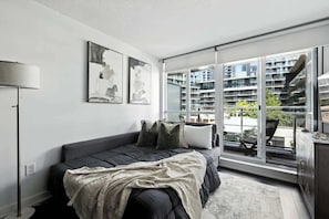 A modern bedroom with a large window, a bed, and a view of a high-rise building. - CityPlace Skyline Retreat Sleeps 5 w Patio! (Toronto)
