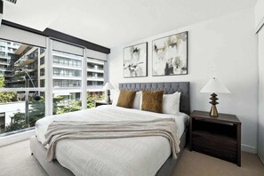 A modern bedroom with a large bed, two bedside lamps, and abstract wall art.