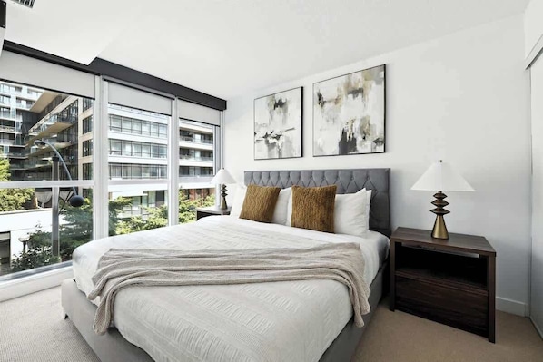 A modern bedroom with a large bed, two bedside lamps, and abstract wall art.