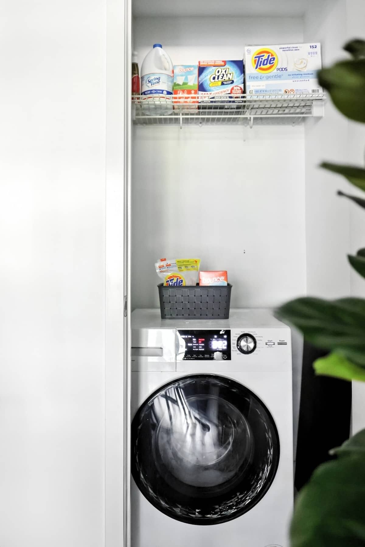 A compact laundry area with a washing machine and detergent products on a shelf.