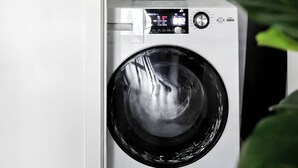 Un espace réduit dédié à la buanderie, comprenant une machine à laver et des produits lessiviels rangés sur une étagère.