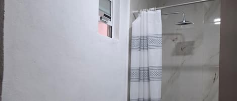 Baño con inodoro, lavamanos, ducha y una ventana pequeña.