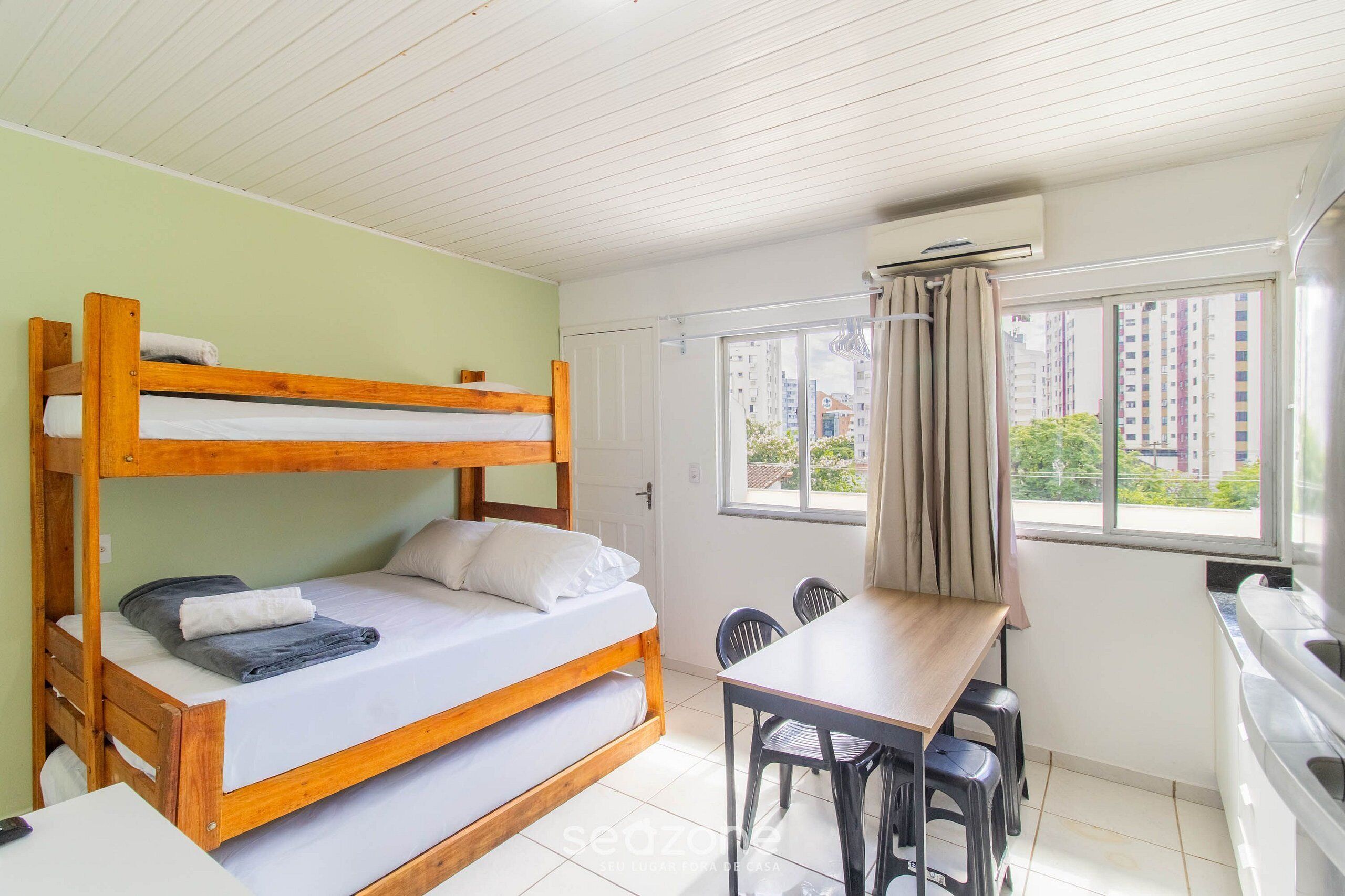 Una cama litera con una mesa y sillas, una ventana con cortinas y un equipo de aire acondicionado.