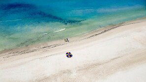An aerial view of a beach with clear water, a sandy shore, and a colorful umbrella. - Siesta Sands - Unit 412 (Siesta Key)
